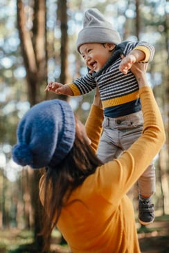 Mother raising her toddler up to the sky in a forest.